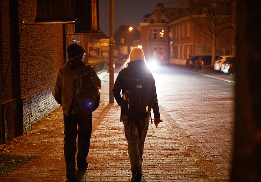 Foto van twee personen die 's avonds over straat wandelen