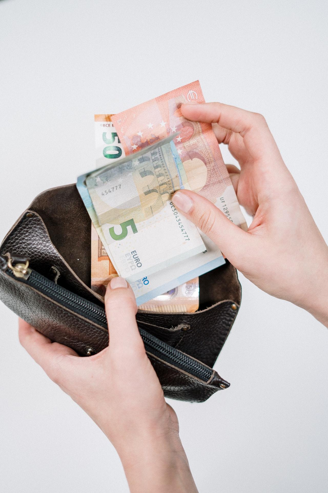 Foto van een hand die briefjes geld uit een portefeuille haalt